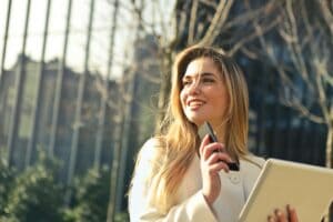 Frau mit Hefter und Handy in der Hand schaut zur Seite